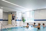 Eine Gruppe Frauen in einem Schwimmbecken macht Wassergymnastik unter Anleitung einer Trainerin, die am Beckenrand steht Eine Gruppe Frauen in einem Schwimmbecken macht Wassergymnastik unter Anleitung einer Trainerin, die am Beckenrand steht